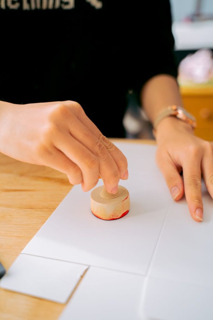 Close-up of a person using a wooden stamp on white paper indoors.